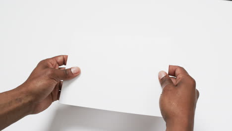 Video-of-hand-of-african-american-man-holding-book-with-blank-pages,-copy-space-on-white-background