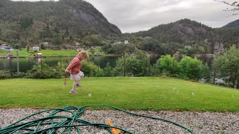 young girl in pink playing with soap bubbles at lawn - holding magic wand in her hand - outdoor playtime by herself - static shot norway