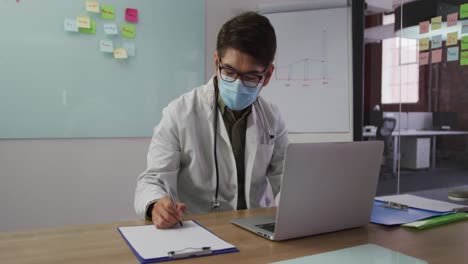 médico masculino asiático con máscara sentado en el escritorio en la sala de reuniones tomando notas