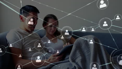 network of connection icons against couple using digital tablet at home