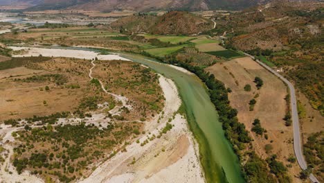 a winding green river cuts through the rolling hills and mountains of albania on a sunny day