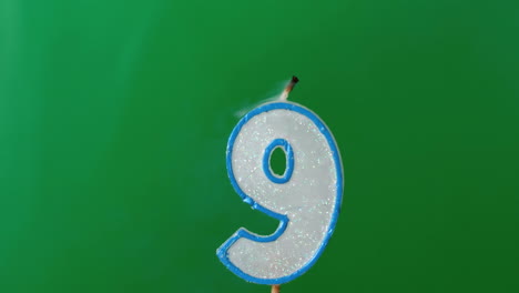 nine birthday candle flickering and extinguishing on green background