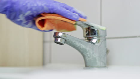 kaukasische hand mit lila handschuh wäscht wasserhahn, um coronavirus zu verhindern