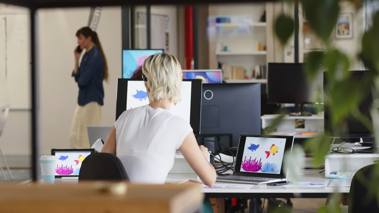 Kvinde designer grafik på flere skærme, arbejder i en kreativ skrivevirksomhed.