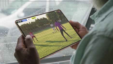 African-american-man-using-tablet-with-diverse-male-soccer-players-playing-match-on-screen