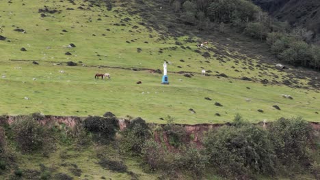 Drone-approaching-the-famous-'El-Cristo'-in-Tafí-del-Valle,-surrounded-by-short-green-grass-and-grazing-horses