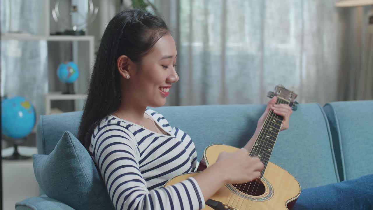 소파 에서 어쿠스틱 기타 를 연주 하는 여자