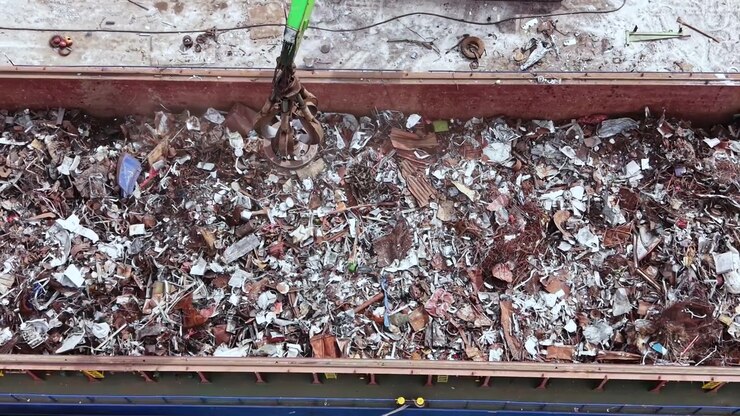 Operai rimuovono scarti metallici da una chiatta in un impianto di riciclaggio alla luce del mattino, mentre i macchinari sono in funzione per smistare i materiali per la lavorazione