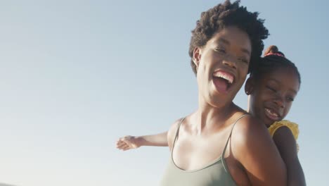 happy african american mother and daughter playing at beach, in slow motion