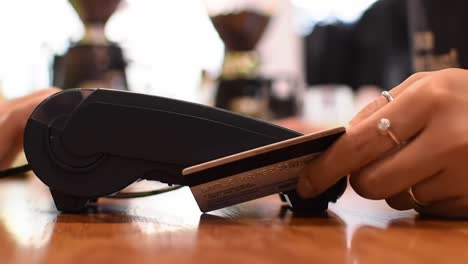 a close-up view of a hand holding a credit card and using a payment terminal at a cafe, highlighting the transaction process and customer engagement