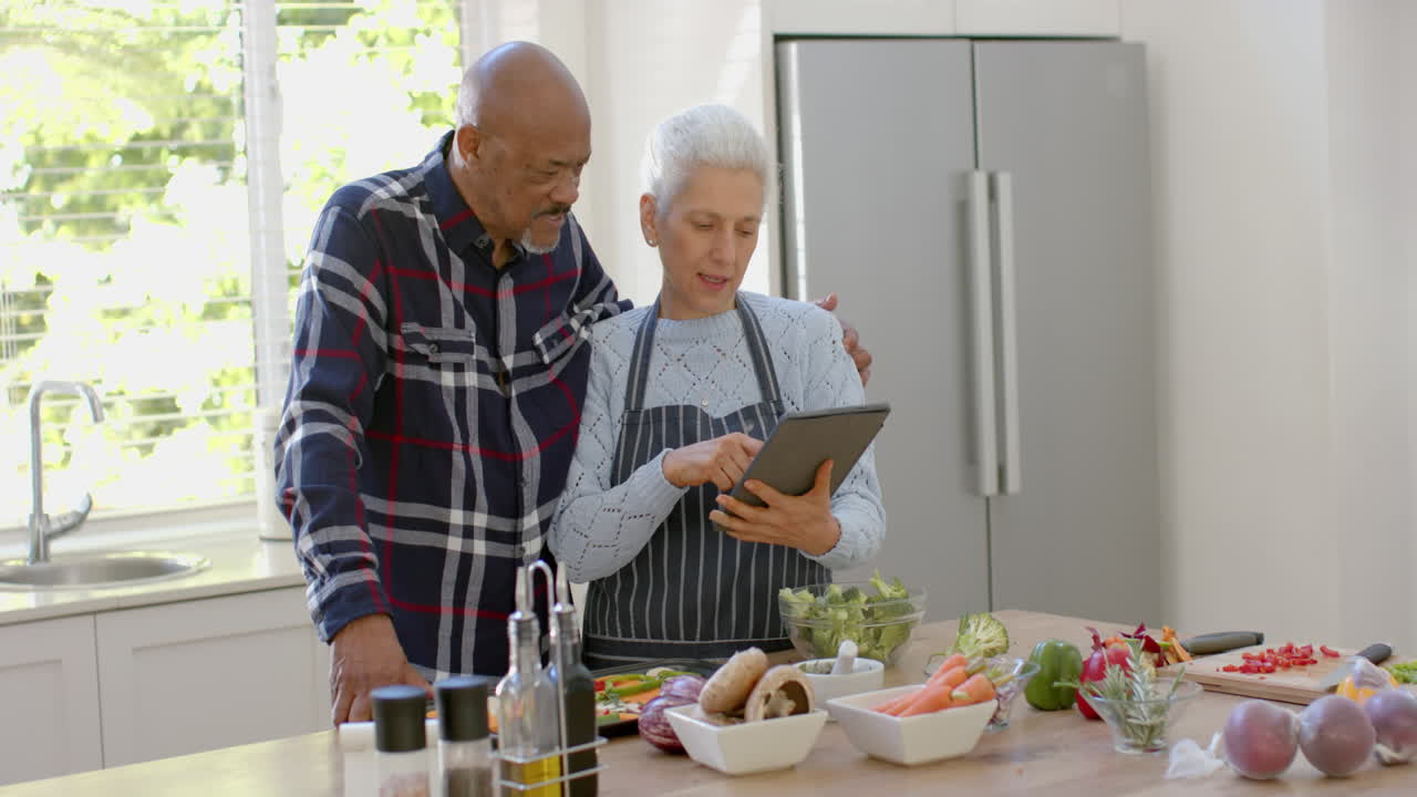 pareja de ancianos feliz preparando verduras, usando tableta en la cocina, espacio de copia, cámara lenta