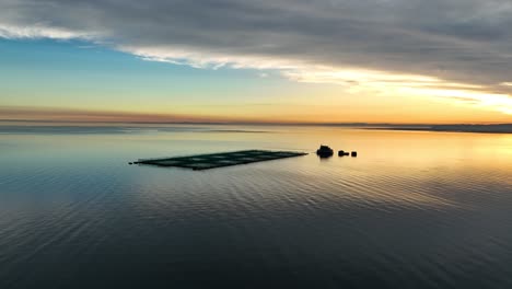 vista aérea de un pontón de cultivo de salmón con una puesta de sol naranja dorada en el horizonte sobre las aguas tranquilas del mar