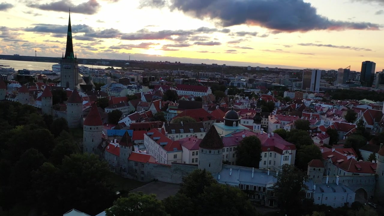 Filmato mozzafiato con drone del Centro Storico medievale di Tallinn al tramonto. L'inquadratura mostra la Collina di Toompea, la Cattedrale di Santa Maria e gli edifici dai tetti rossi sotto un cielo drammatico di nuvole rosa e arancioni.