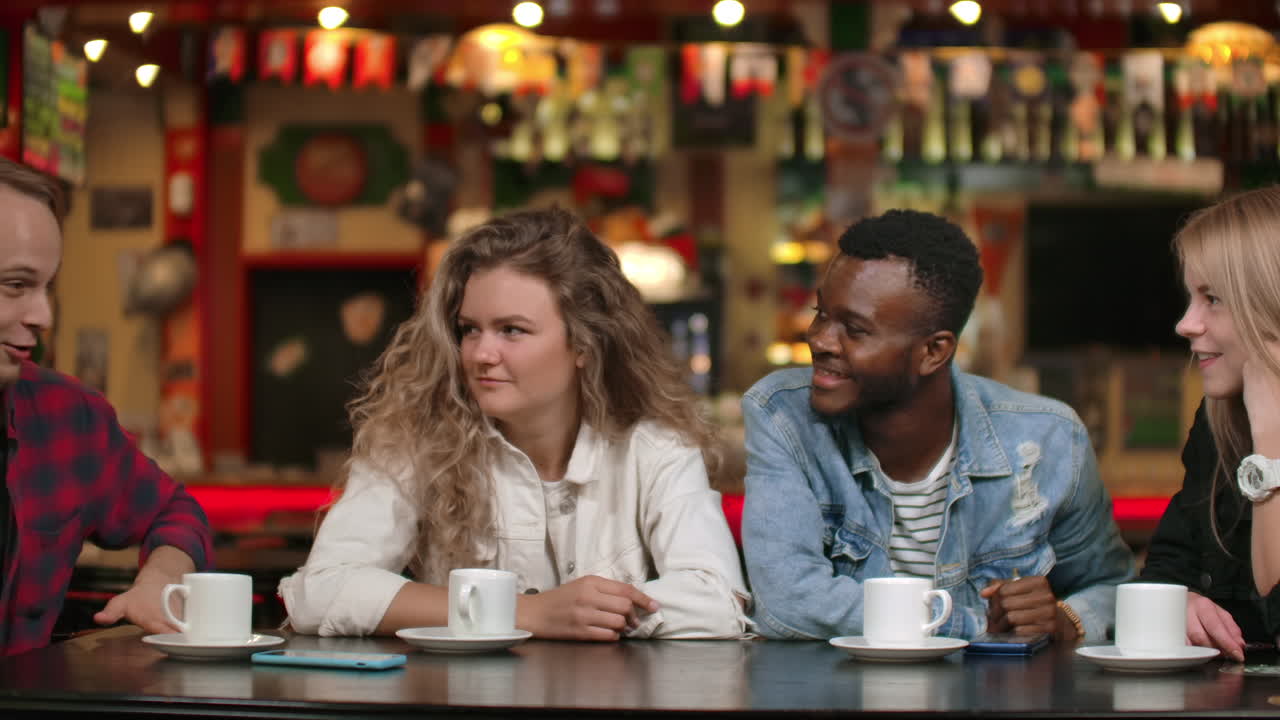 un hombre con una camisa cuenta una historia a sus amigos dos chicas y un afroamericano están escuchando y riendo. un grupo de amigos pasan tiempo juntos. reunión de estudiantes.