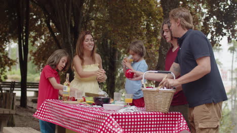 Toma-Manual-De-La-Familia-Poniendo-Comida-De-La-Canasta-En-La-Mesa-Durante-Un-Picnic-En-El-Bosque