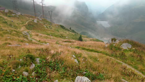 scenic view of meadows in mountain alps with misty valley in the background, passo san marco, northern italy - aerial drone shot