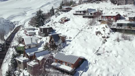 Aerial-orbit-of-the-European-style-houses-and-cabins-built-on-the-edge-of-a-completely-white-and-snowy-hill-on-a-sunny-day,-Chile