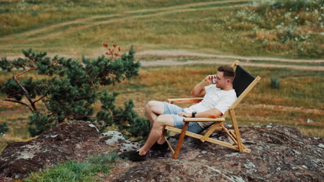 man having rest in the nature. caucasian male sits in a comfortable folding chair on the rock speaking on the phone. top view.
