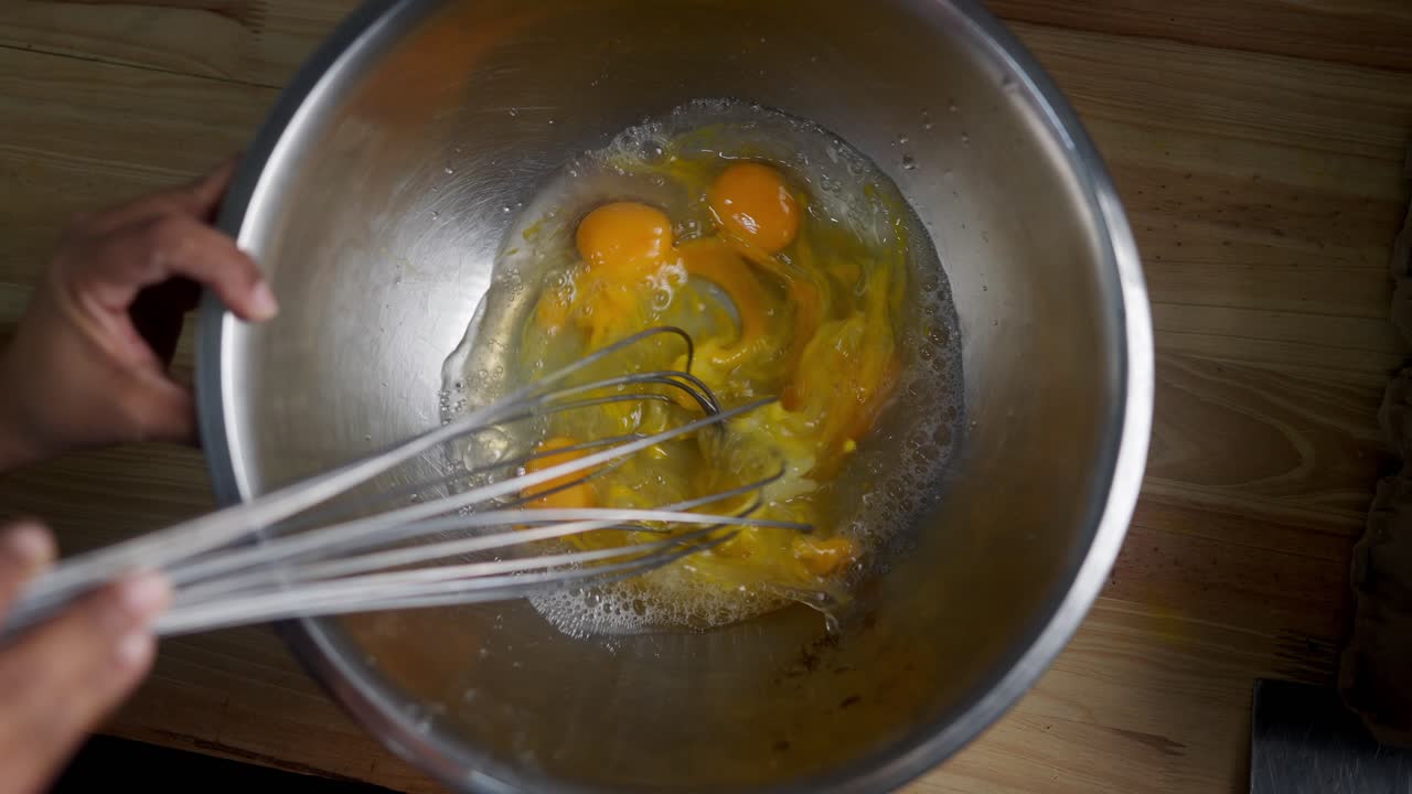 Cinematic Top view of a balloon whisk scrambling eggs in a metal bowl for a gourmet recipe in a fancy restaurant