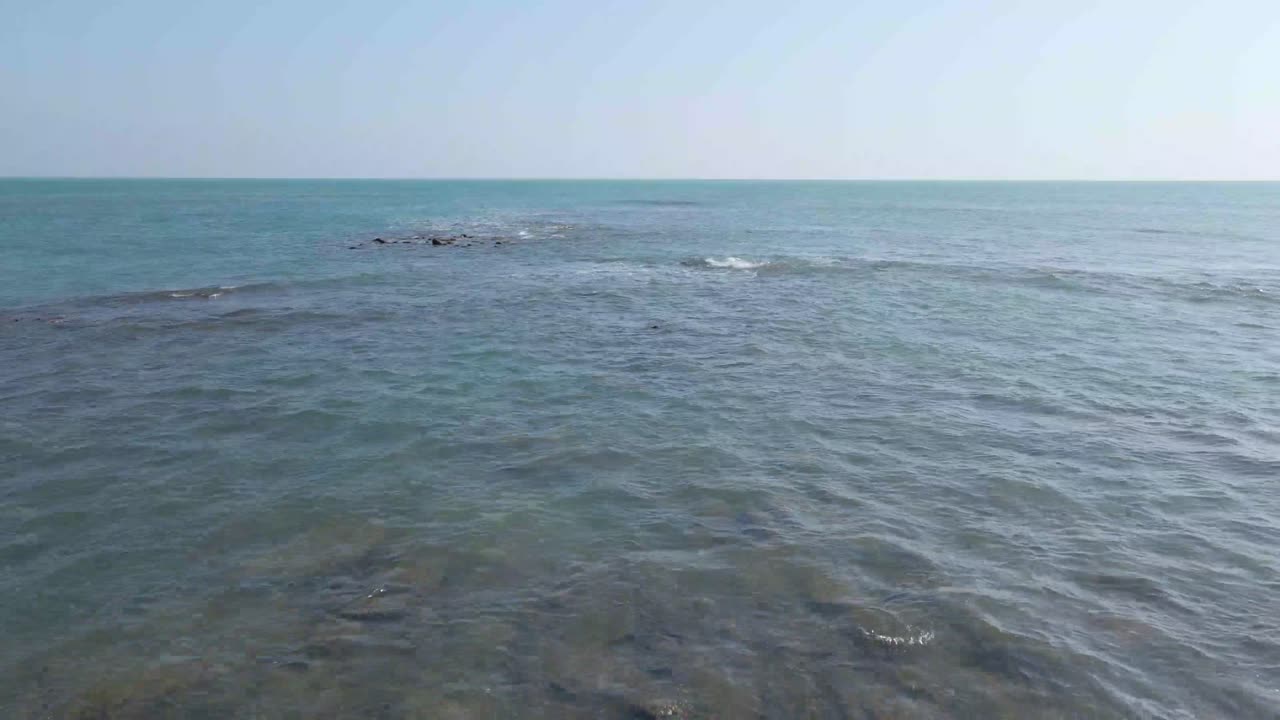 Seascape of rocky coast with vast blue ocean in a tropical island. Gentle waves breaking on corals. Bluish sky over the horizon. Drone flying forward over corals and sea water