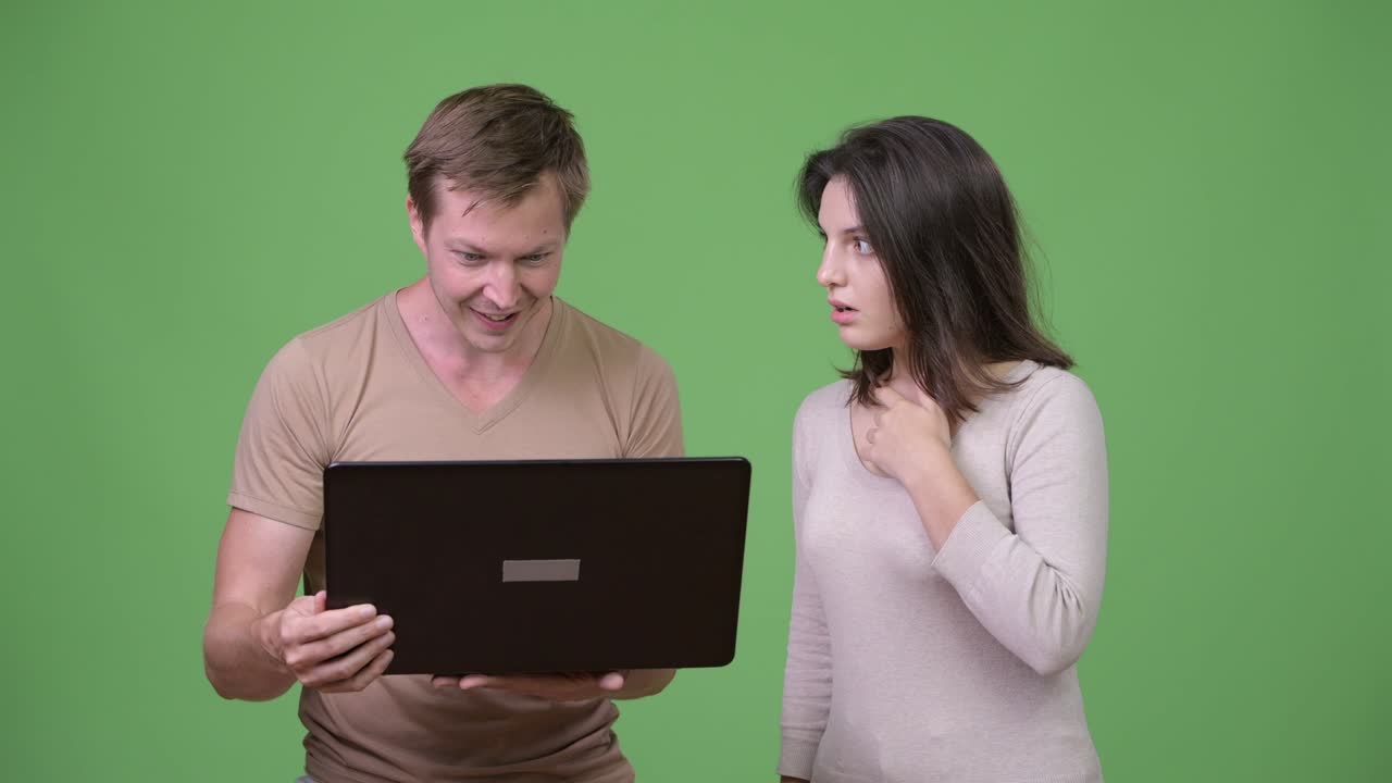 Young man using laptop with young woman looking shocked