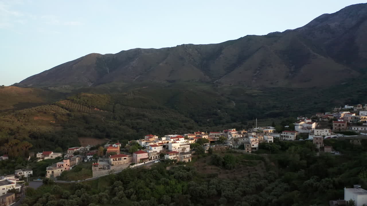 alejamiento aéreo del pueblo griego tradicional en grecia al atardecer con montañas en el fondo