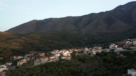 Alejamiento-Aéreo-Del-Pueblo-Griego-Tradicional-En-Grecia-Al-Atardecer-Con-Montañas-En-El-Fondo