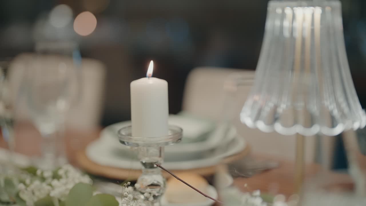 Close-up of a white candle burning in a glass holder on a beautifully decorated dinner table with soft focus