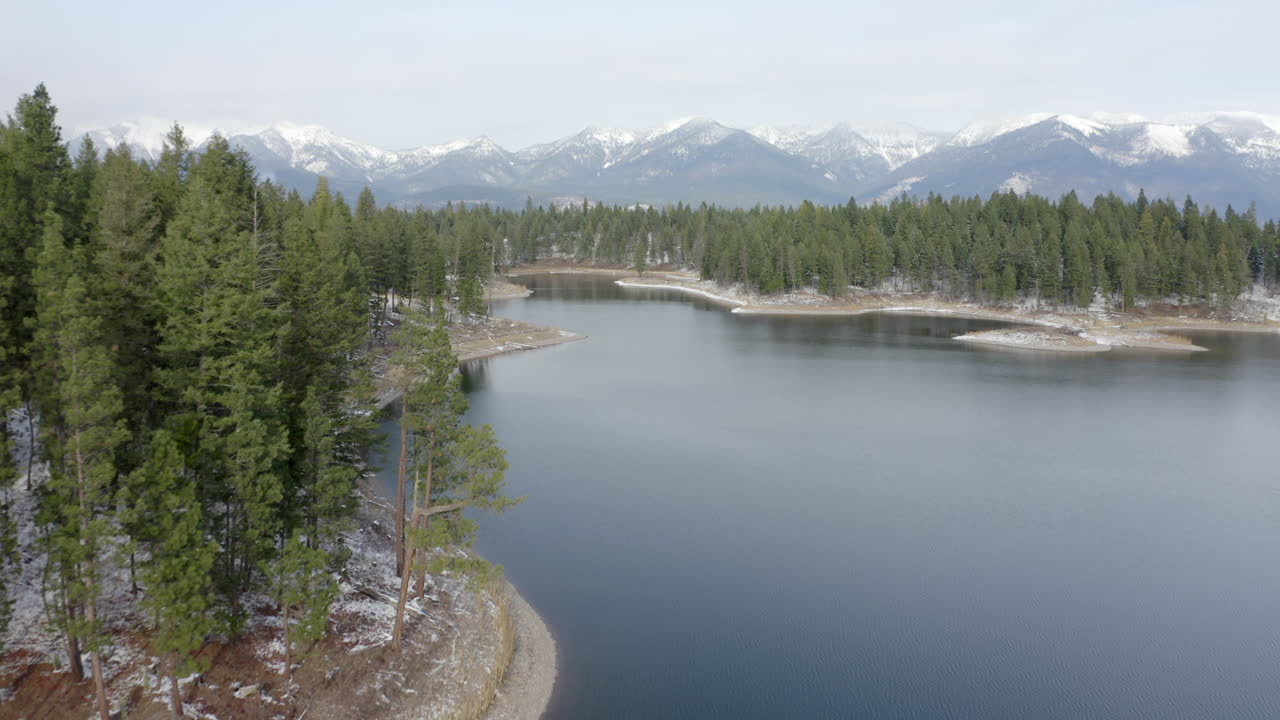 sobrevuelo aéreo de un lago remoto en el desierto de montana con montañas cubiertas de nieve en el fondo