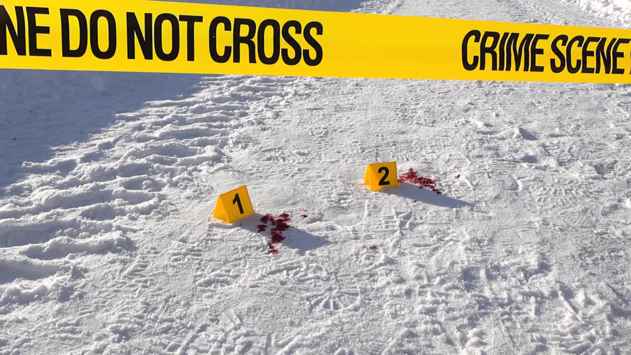 Low angle view of crime scene tape in foreground pulled across snow covered road. Numbered evidence markers beside blood spatter. Violent winter incident on snowy ground with boot prints, tire tracks