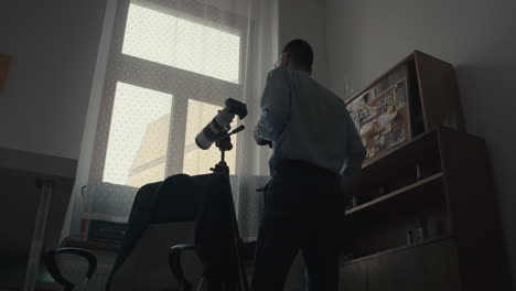 spy looking through window, watching suspect and using binoculars and camera, low angle interior view