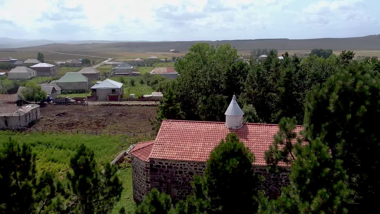 Experience the tranquility of a village surrounded by nature, featuring traditional homes, green fields, and wide-open landscapes under a clear blue sky