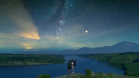 the two tourists standing on the mountain top above night river