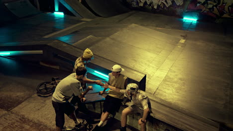 Tired-teenage-men-resting-after-sport-training-at-night-skate-park.