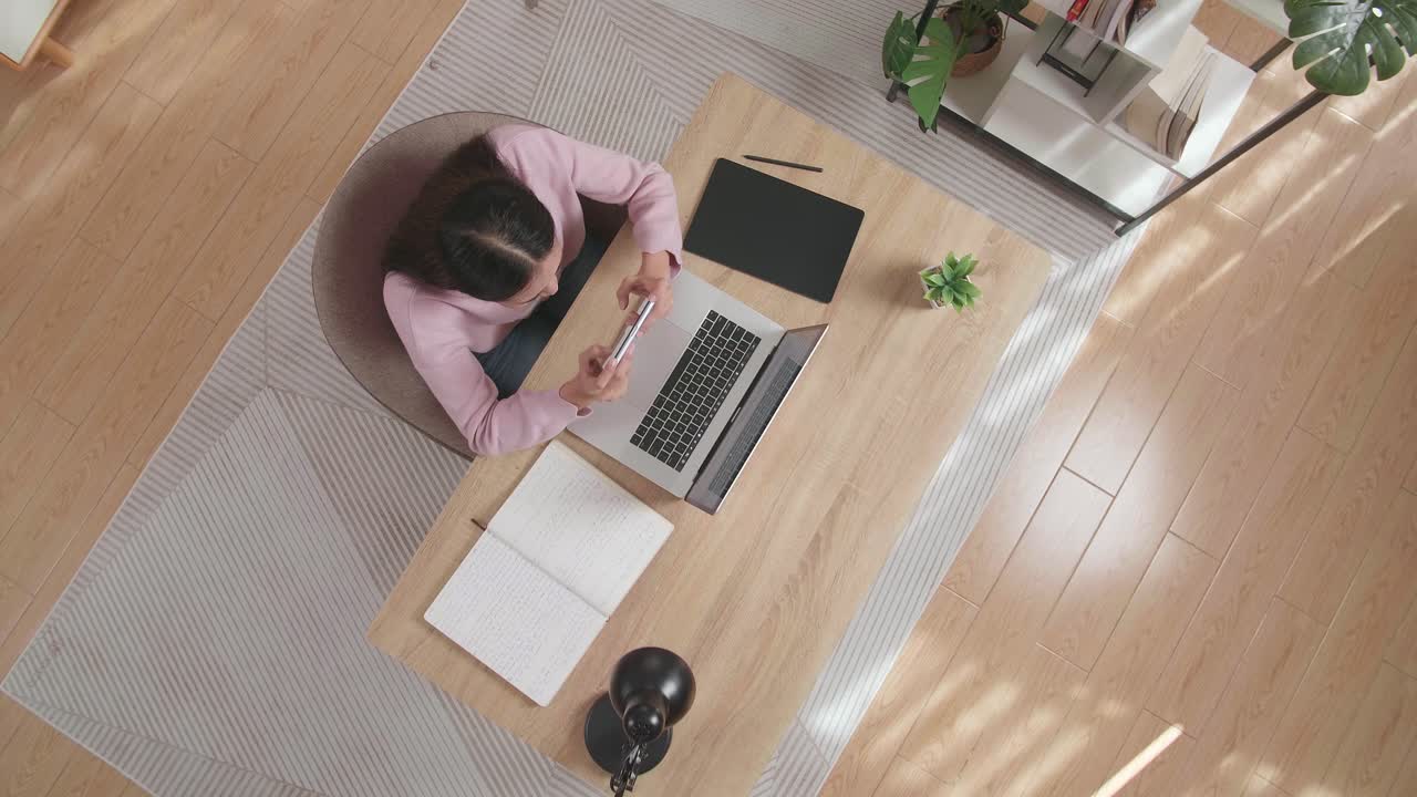 Top View Zoom Out Shot Of A Woman Playing Game On Smartphone While Sitting At The Wooden At Home