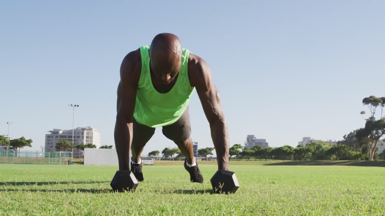 Fit african american man exercising outdoors doing press ups holding dumbbells