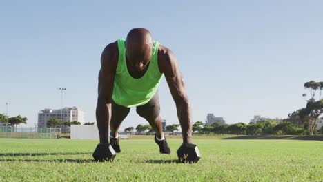 fit african american man exercising outdoors doing press ups holding dumbbells