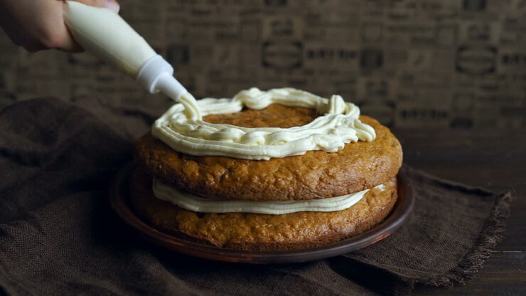 Preparazione di un dolce. Chef versa la panna sulla torta di carote. Realizzazione di torta di carote.