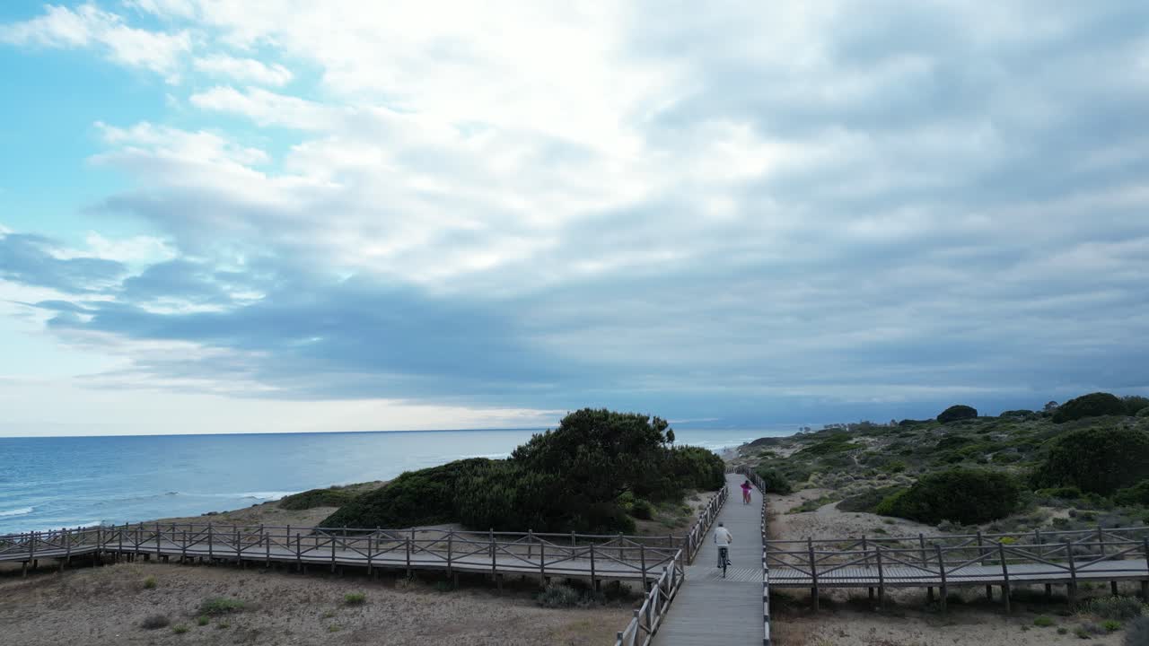 Drone video of a beach in southern Spain, where people enjoy taking a walk along a wooden path along the beach.