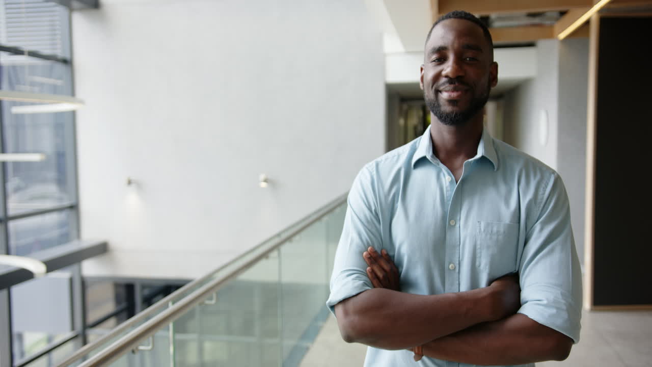 Homme d'affaires souriant se tenant avec assurance les bras croisés dans un couloir de bureau moderne, espace pour texte