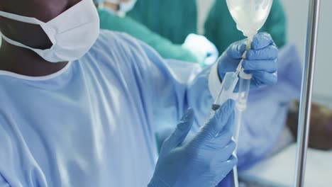 Video-of-african-american-male-surgical-assistant-preparing-drip-during-operation-in-theatre