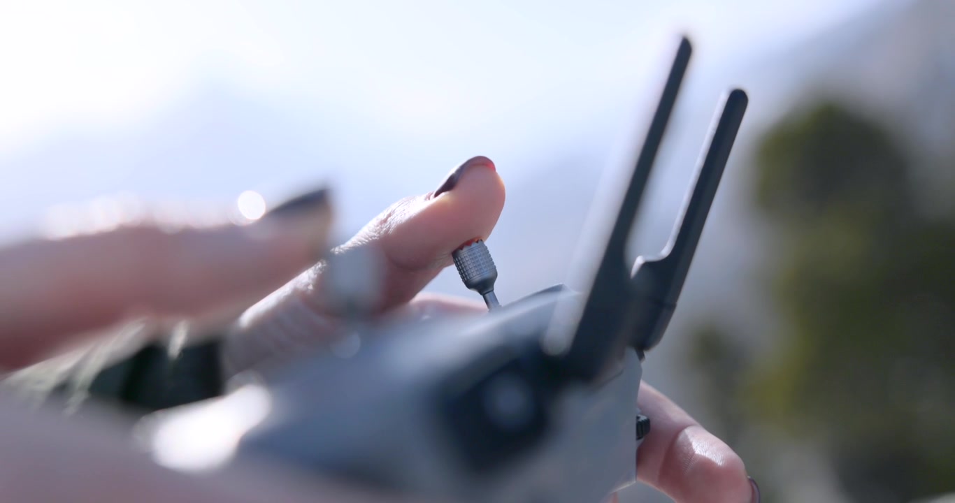 Polpastrelli con smalto scuro girano con attenzione una piccola manopola su un telecomando pieghevole per drone in piena luce esterna