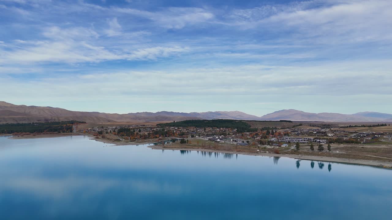 Drone footage captures Lake Tekapo's serene waters and nearby town under clear skies, highlighting natural beauty and tranquility