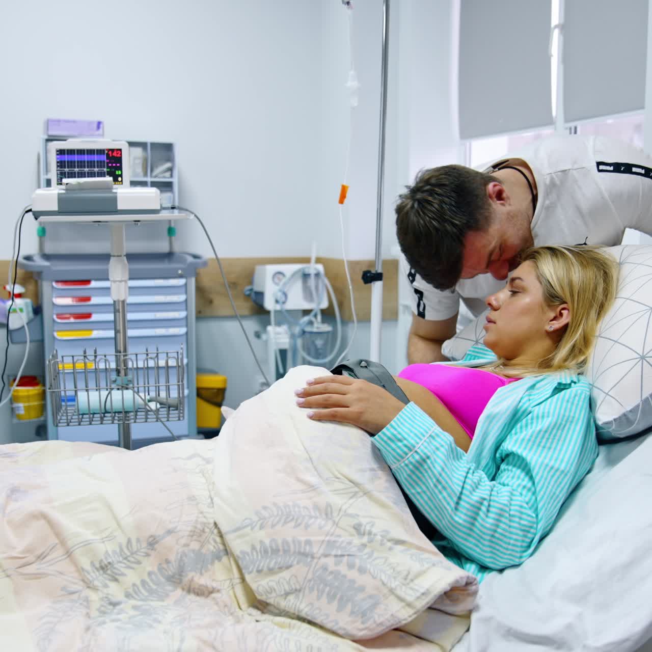 Pregnant lady is getting ready for delivering a baby. A cardiotocography belt is on woman's belly. Caring man soothing his wife