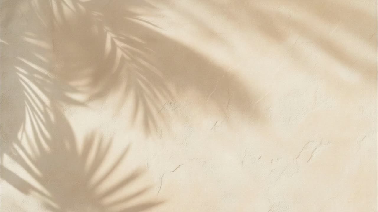 Soft, dreamy shadows of palm leaves dance on a textured beige wall, creating a serene, tropical