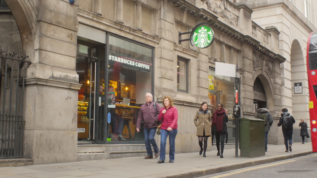 Young student tourists leaving a coffee shop with a red double-decker bus passing.