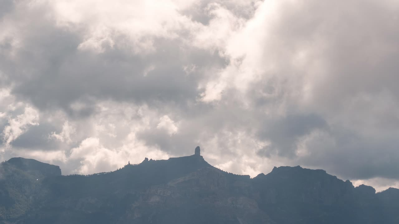 Dramatic timelapse of Roque Nublo silhouetted against a cloudy sky. The iconic volcanic rock stands tall as clouds drift by. Perfect for nature, travel, and atmospheric projects.
