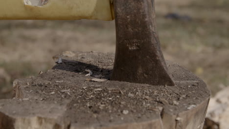 wide macro footage of the head of an axe sticking into a log with debris flying