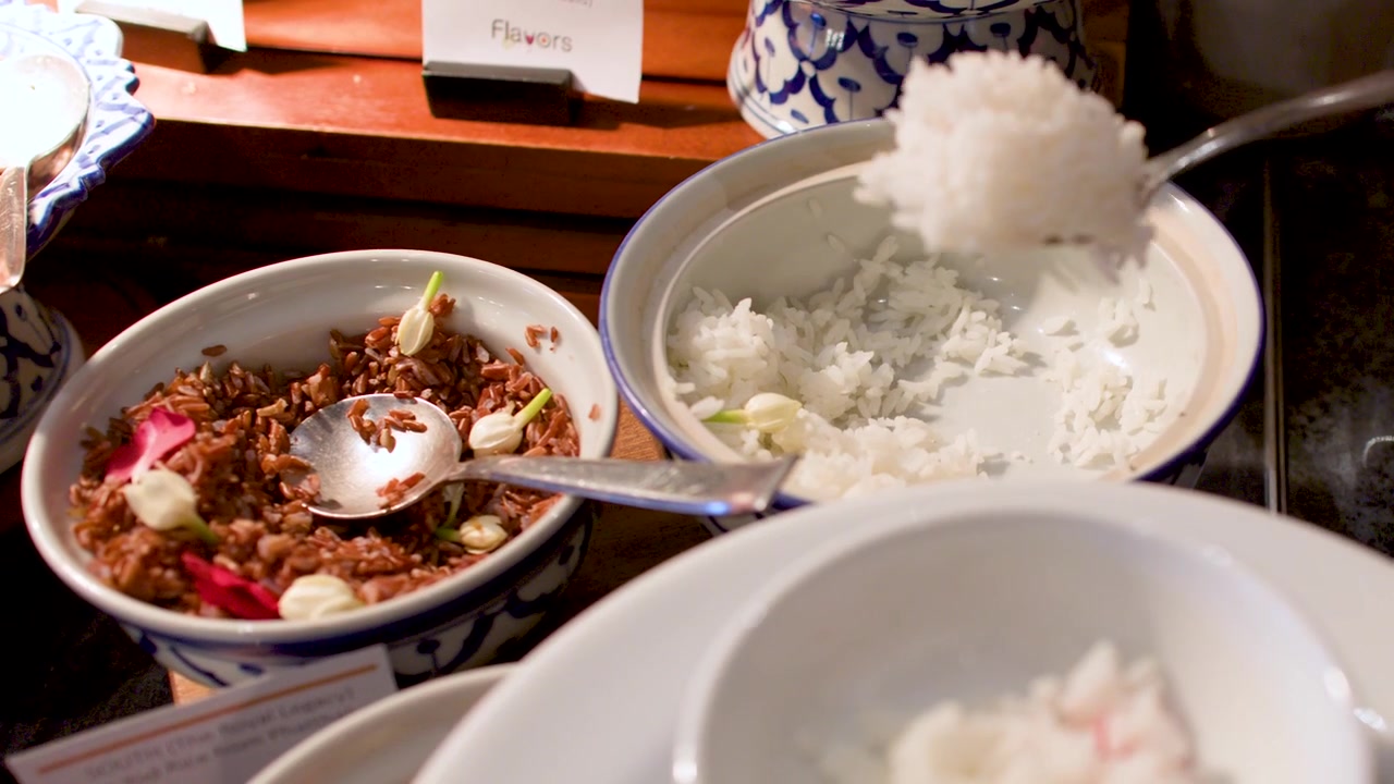 伝統的なタイ料理の食事中に、白い器から冷やしたジャスミンライスをすくう人