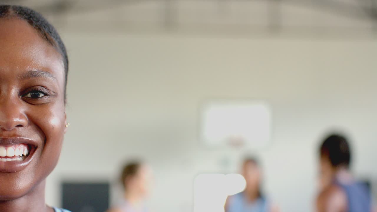 Smiling woman in basketball court with teammates in background, enjoying practice, copy space